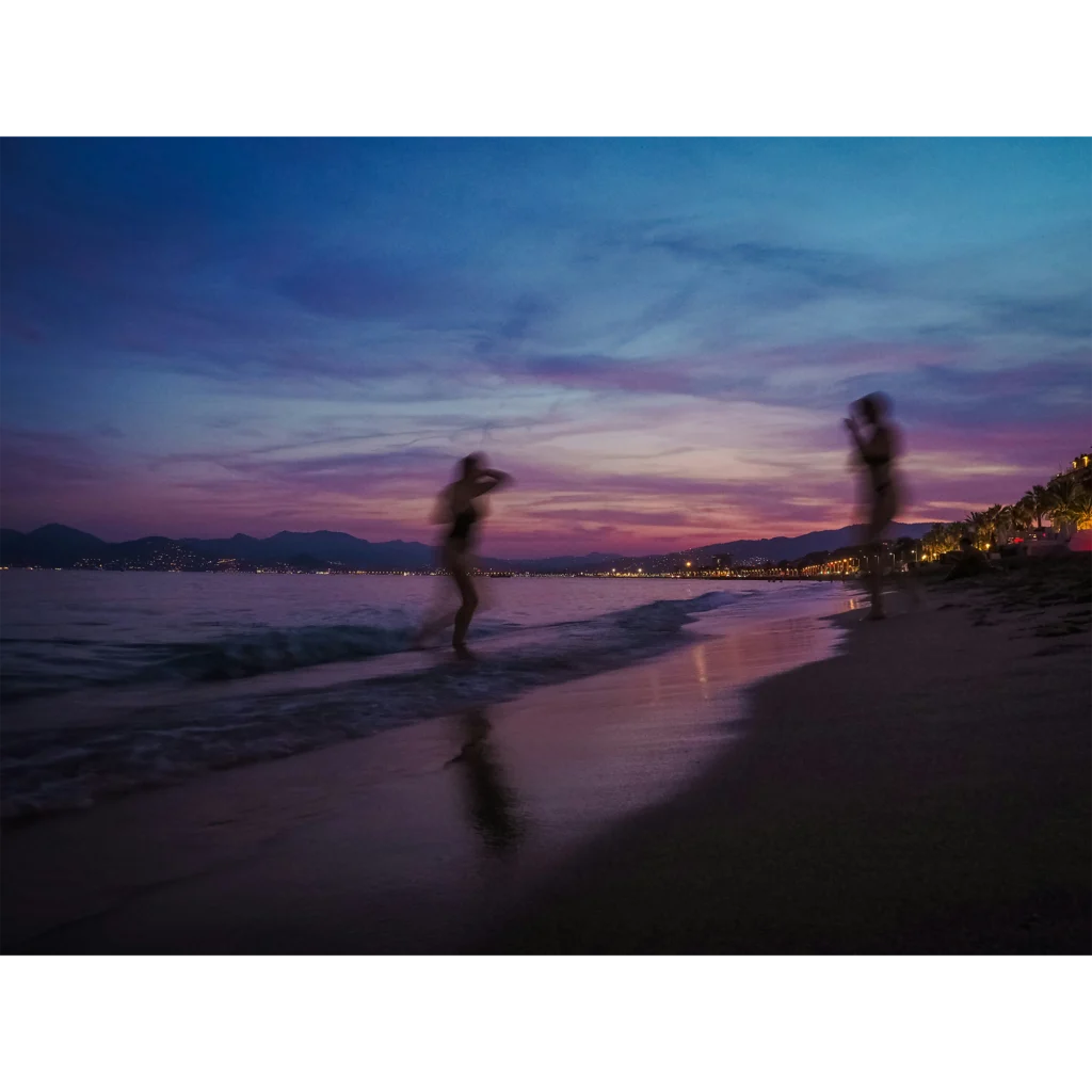 Ein lila, blauer Sonnenuntergang am Strand. Die Shillouette zweier Menschen ist zu sehen